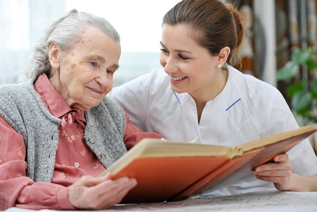 A caregiver looking through a photo album with a smiling elderly woman at home
